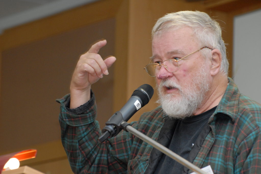 A man with a beard and glasses is speaking at a microphone.